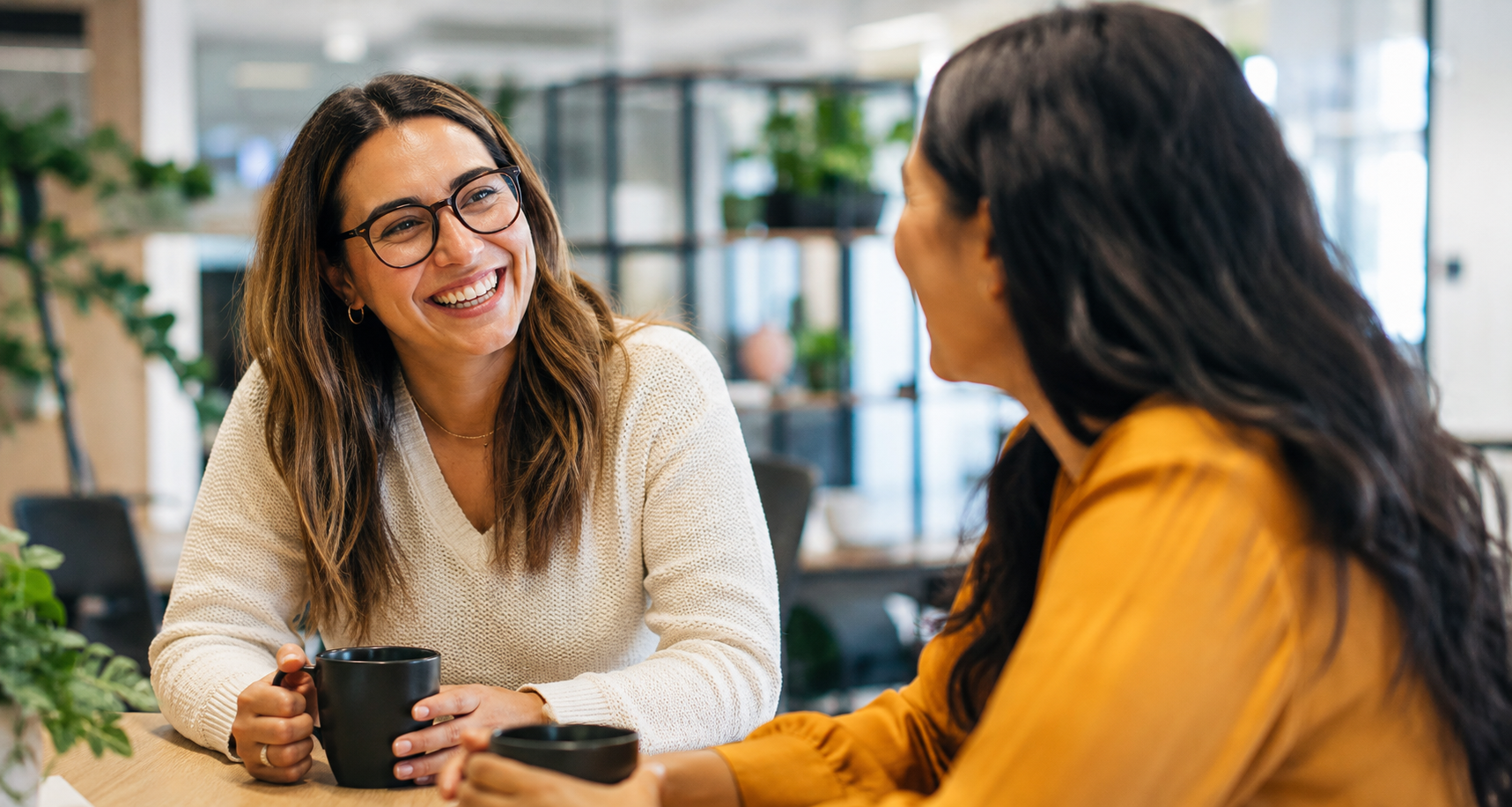 Two coworkers laughing together over coffee during an easy, unplanned conversation